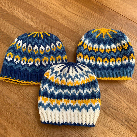three bulky weight knitted hats in shades of yellow, blue, and white