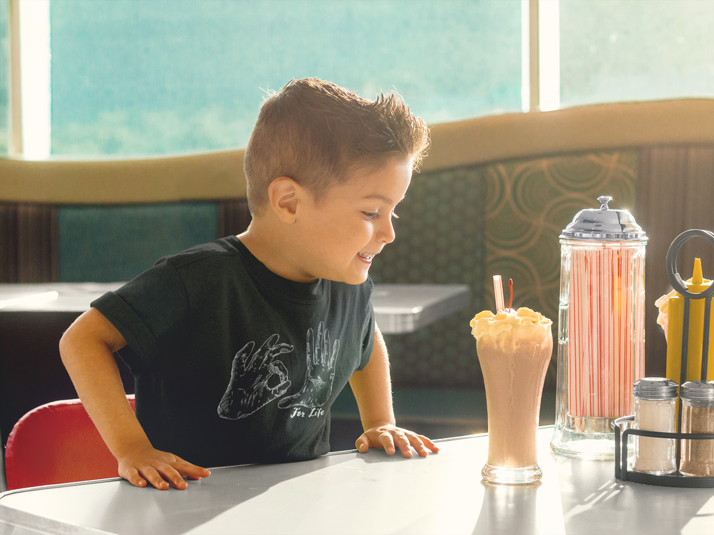 image of boy at a table with a milkshake wearing a black shirt with a 305 for life graphic