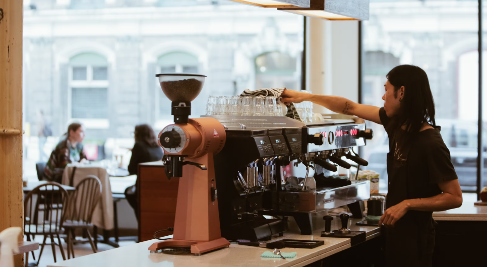 A barista prepares coffee in a Lantana cafe. People are in the background eating at their table.