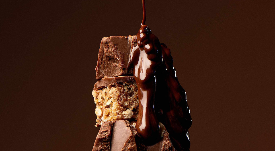 Close-up of a stack of Prodigy's chocolate bars in front of a brown background, with melted chocolate dripping down the sides from above.