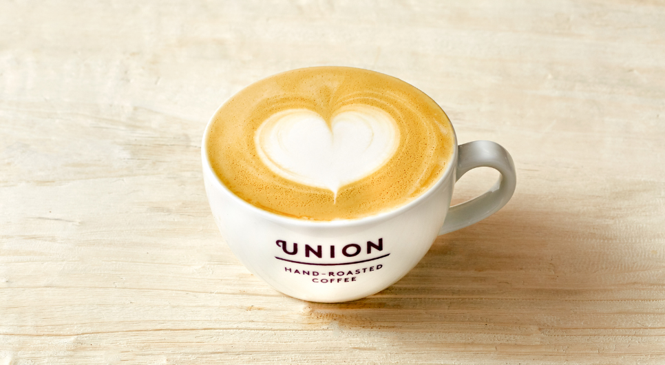 A white cup of coffee with the purple Union logo on the front, with 'hand-roasted coffee' in purple font underneath it.
