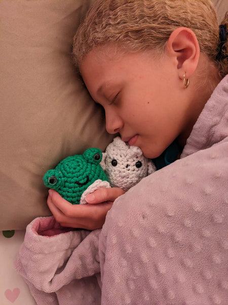 A young girl sleeping with her handmade green frog and white owl amigurumi plushies