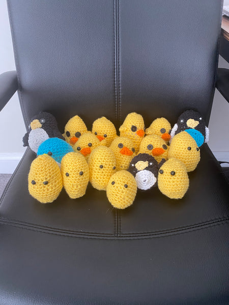 A number of blue and black penguin crochet plushies and yellow chick crochet plushies sitting on a black office chair