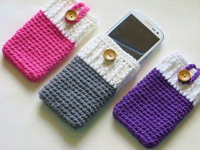 Pink and white, gray and white and purple and white phone cozies with buttons. The middle phone cozy has a white phone in it