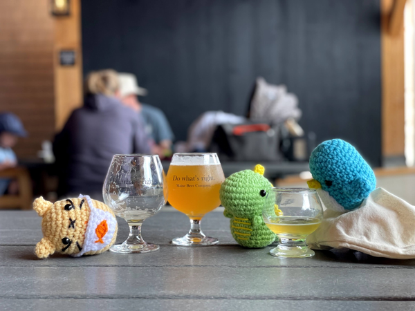 Penguin, dinosaur and cat amigurumi plushies on a table with two glasses of beer