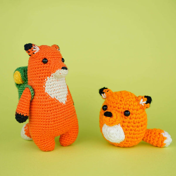 Larger crocheted fox with a backpack on next to a smaller crocheted fox.