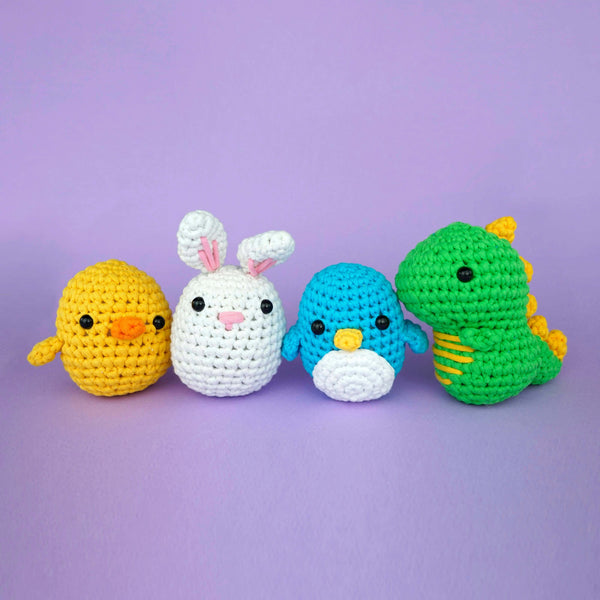 Stuffed crochet penguin with a stuffed crochet bunny and chick on his right, and a stuffed crochet dinosaur on his left.