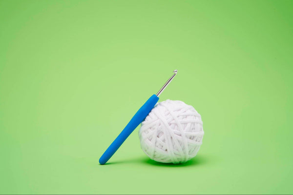 A crochet hook with a blue handle leans on a ball of white yarn