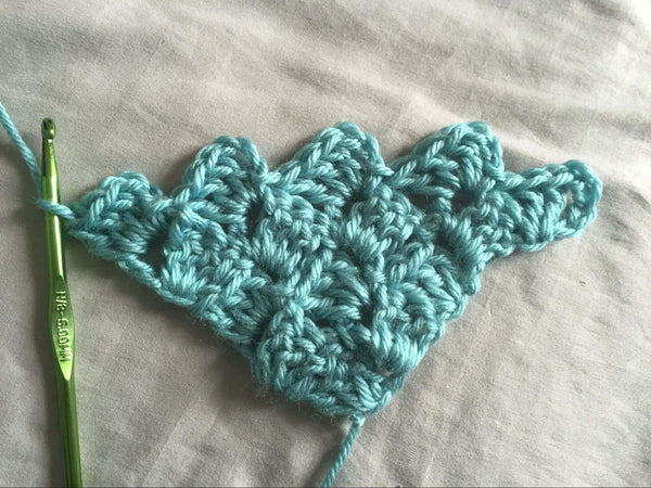 Green crochet hook looped into aquamarine yarn