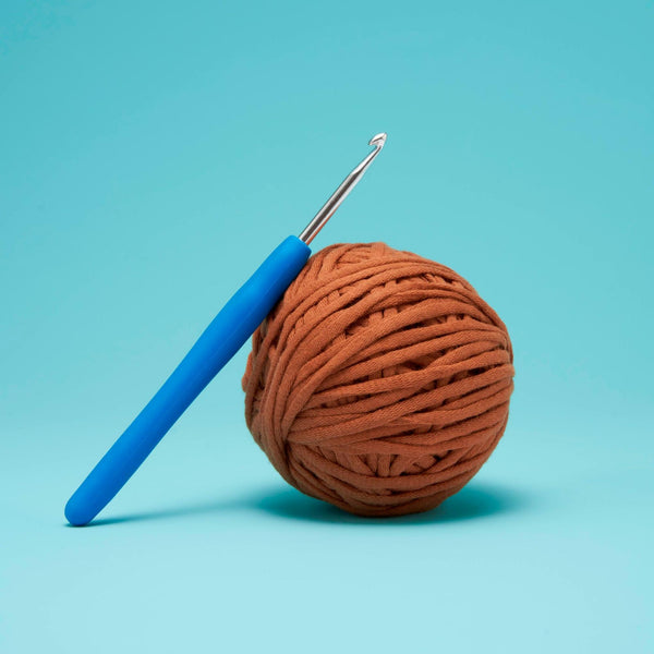 A crochet hook with a blue handle leans on a ball of brown yarn