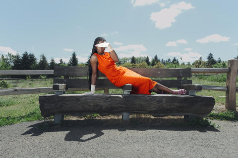 Naomi lays on a log bench with an orange Rachel Comey dress and pink gloves