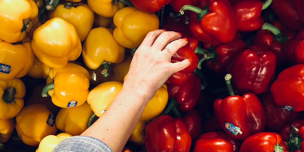 a woman selecting red and yellow bell peppers from a supermarket