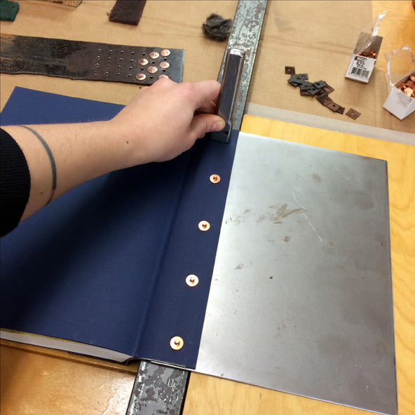 setting copper rivets in a leather book spine to attach cover