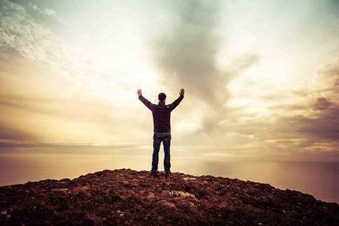 Man standing on a hilltop with hands raised to the sky