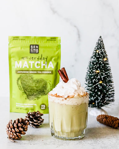 Photo of egg nog made with matcha green tea powder, with festive Christmas tree and pine cone decorations in background.