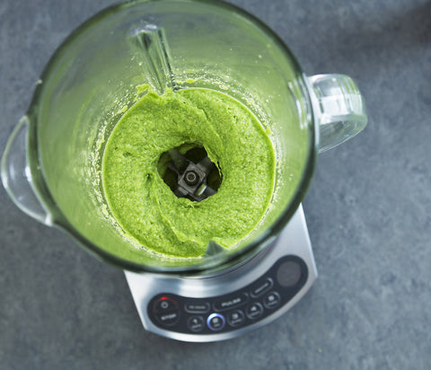 A photo of a clear glass blender carafe containing a green tea smoothie mix