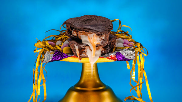 A chocolate sweet pastry pie filled with a Cadburys Creme Egg. Placed on a golden cake stand, cut open and oozing the gooey filling. Surrounded by mini Cadbury Creme Eggs. Happy Easter!