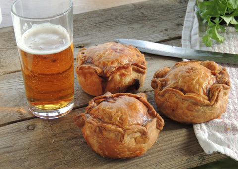 three pork pies on a picnic table with a glass of beer