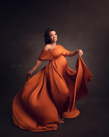 brunette model poses in a studio wearing a cape made of silk in cognac color.