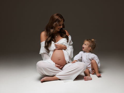 mother and daughter posing at the studio. they have matching outfits in white color. the mom wears a chiffon set with pants and top.