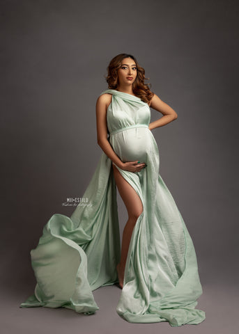 brunette pregnant model poses in a studio wearing a silky scarf in mint green color wrapped around her body as a one shoulder dress.