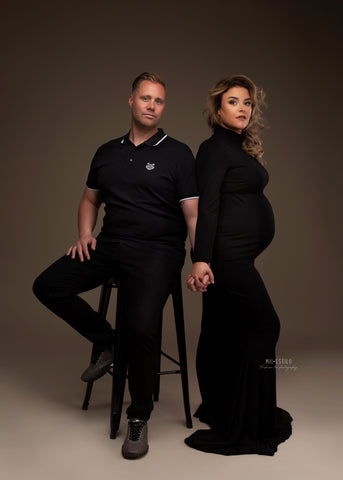 pregnant model poses together with her partner. they are both wearing black - she wears a long dress with turtle neck and long sleeves.