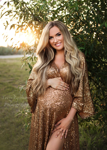 blond model poses outdoors wearing a sequin golden dress with a low v cut neckline. 