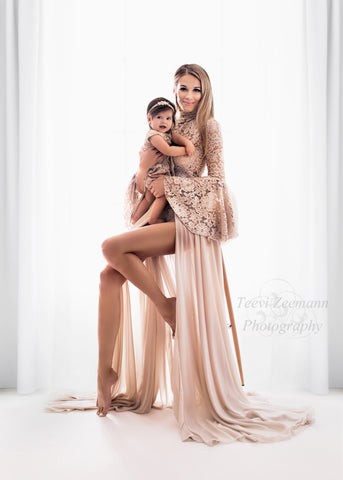 mère pose avec sa fille dans un studio. elles portent toutes les deux une tenue en dentelle et mousseline de couleur rose.