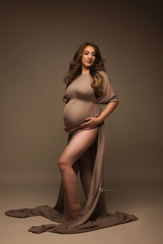 dark blond pregnant model poses in a studio wearing a chiffon cape in espresso color. her leg can be seen through the side split on the skirt. 