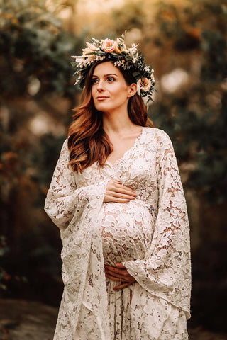 Das schwangere Model posiert im Freien mit einem langen weißen Spitzenkleid und einer Blumenkrone