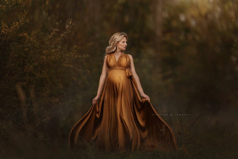 dark blond pregnant model poses outdoors wearing a silk dress in cognac color.