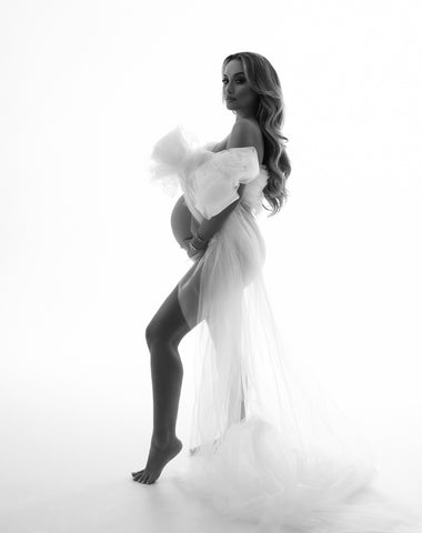 black and white photo of a pregnant model posing wearing only a tulle scarf tied on her chest as a bow. 