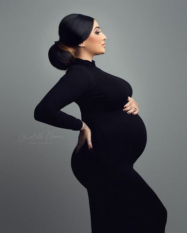 modèle enceinte pose sur le côté montrant sa silhouette - elle porte une longue robe noire à manches longues et un col roulé.