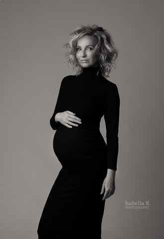Das schwangere Model posiert in einem langen, engen schwarzen Kleid mit Rollkragen und langen Ärmeln.