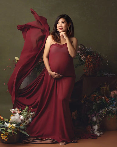 Brünettes schwangeres Model posiert in einem Studio und trägt einen Chiffonschal in Bordeaux, der um ihren Körper gewickelt ist.