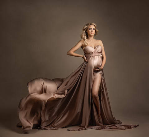 blond pregnan tmodel poses in. studio wearing a pink silky maternity dress featuring a strapless neckline and an adjustable sweetheart top. 