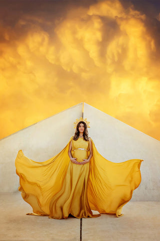 Das brünette schwangere Model posiert draußen vor der Pyramide und trägt einen langen senffarbenen Umhang aus Seide.