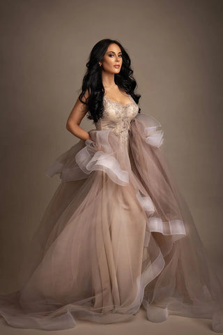 Brünettes Model posiert in einem Studio während eines Glamour-Fotoshootings. Sie trägt ein langes Tüllkleid mit vielen Brautspitzendetails am Oberteil.