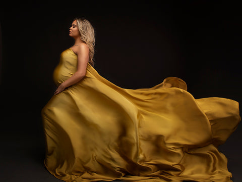 The model is wearing a scarf around her body. The silky material adds a luxery look. The model is pregnant and has long blonde hair. She is covered with the long piece of fabric