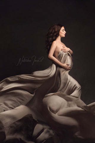 pregnant model poses on her profile holding a silky scarf in sand color against her body.