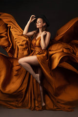 Das Model posiert in einem Studio und trägt ein cognacfarbenes, seidiges fliegendes Kleid