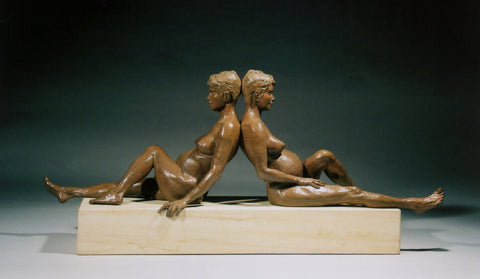twin and pregnant female figures sit back to back, leaning against one another.  they sit on a long limestone base, one hand curving around the edge of the stone.  One knee up and moving modestly over the other leg slightly... bronze sculpture by Kelly Borsheim