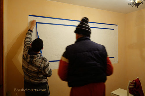 Two men assist in marking straight and horizontal line on the wall for the mural.