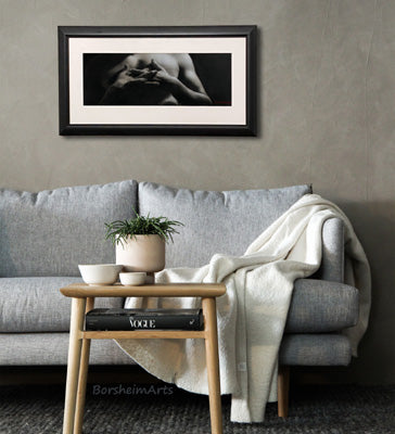 framed charcoal drawing of man's intertwined fingers resting on his chest in a grey living room scene