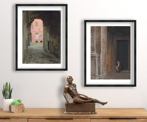 Bronze nude man sculpture sits on a dresser with two pastel drawings of Siena and Bologna hanging above the art.