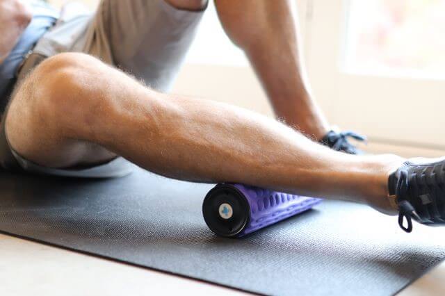 Homme utilisant un rouleau en mousse pour masser les muscles du mollet.