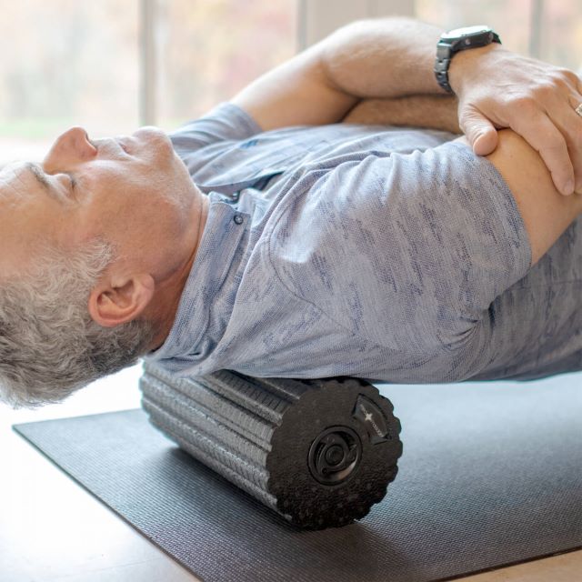 Man using foam roller to roll upper back.