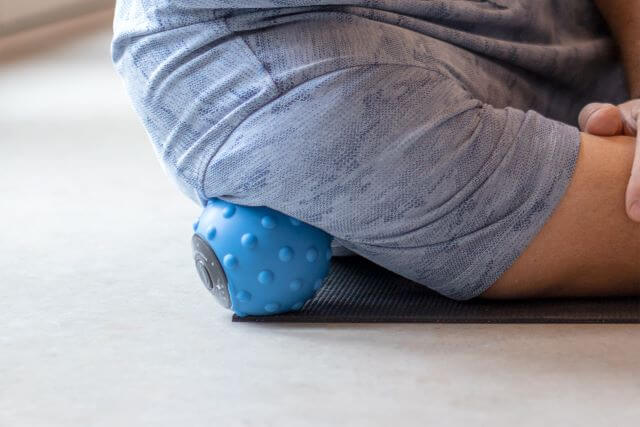 Person using massage ball to roll shoulder muscles.