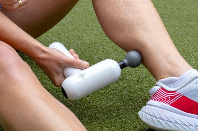 Person using massage gun on calf muscle.