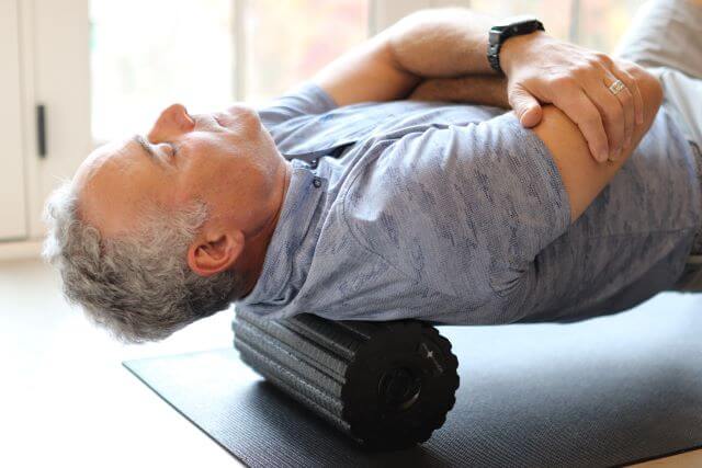 Man using foam roller on upper back.